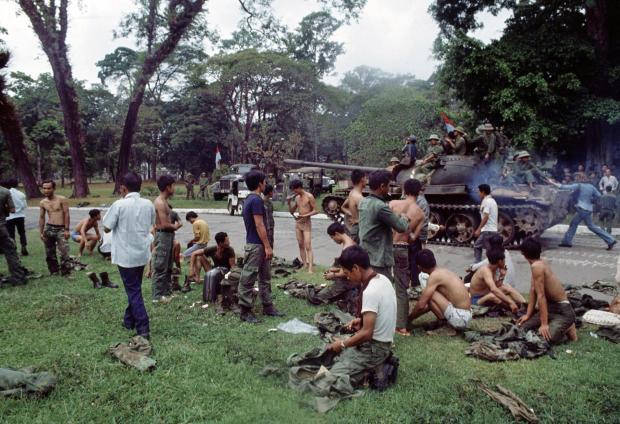 FILE- As victorious North Vietnamese troops ride past on a tank, defeated South Vietnamese troops discard their uniforms in Saigon, April 30, 1975, the day the South Vietnamese capital fell to communist forces, ending the Vietnam War. (AP Photo/Yves Billy, File)