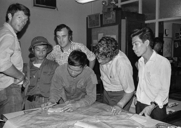 FILE- The last three staffers in The Associated Press' Saigon bureau, reporters Matt Franjola, left, Peter Arnett, rear, and George Esper, second from right, are joined by two North Vietnamese soldiers and a member of the Viet Cong on the day the government of South Vietnam surrendered, April 30, 1975. One of the soldiers is showing Esper the route of his final advance into the city. (AP Photo/Sarah Errington, File)