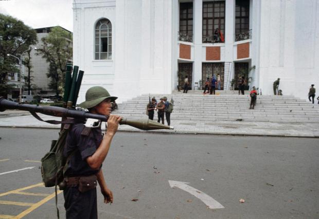 FILE- A communist fighter carrying a rocket-propelled grenade passes comrades on the steps of the National Assembly (Parliament) building in Saigon on April 30, 1975, as South Vietnam surrendered to North Vietnam, ending the Vietnam War. (AP Photo/Yves Billy, File)